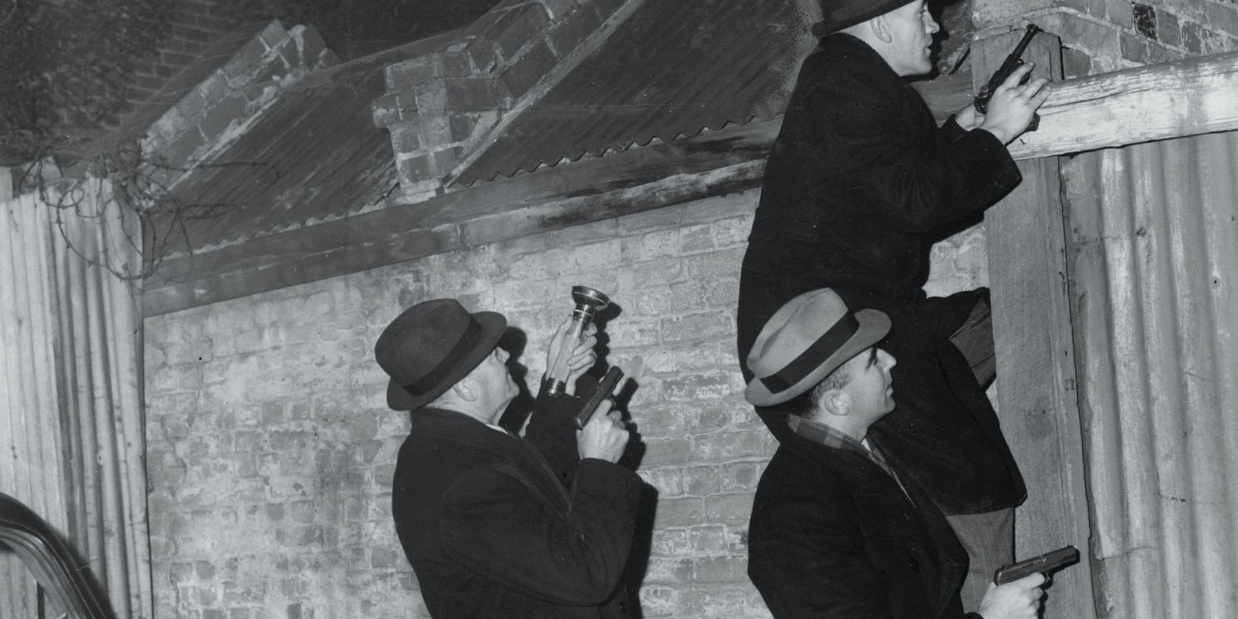 Photo of detectives climbing over a wall at nighttime