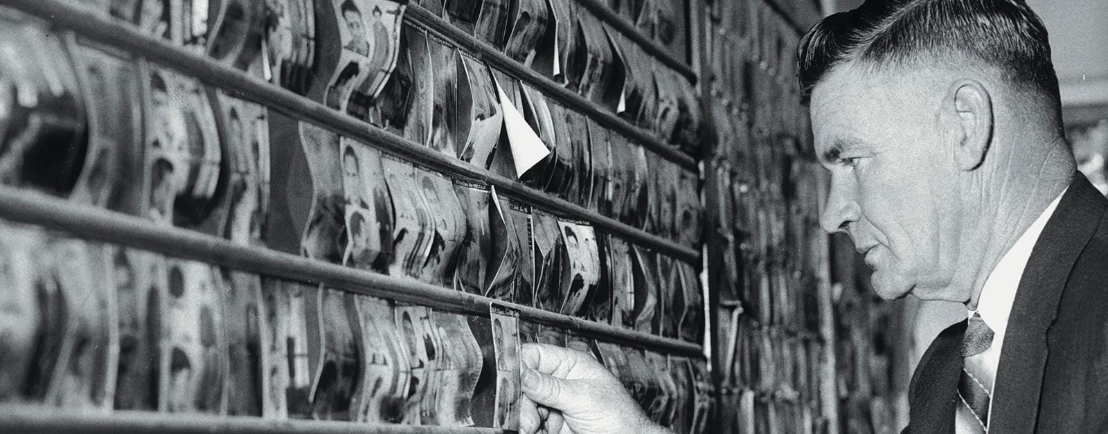 Photo of a detective looking at a wall of mug shots